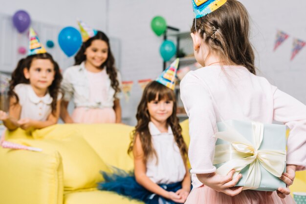 Vista posterior de una niña que oculta un regalo de su amigo en la fiesta de cumpleaños