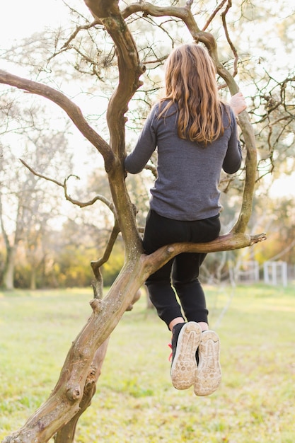 Foto gratuita vista posterior de la niña sentada en la rama de un árbol en el parque