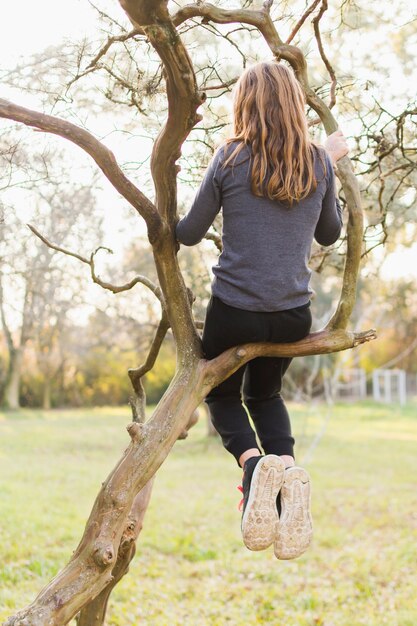 Vista posterior de la niña sentada en la rama de un árbol en el parque