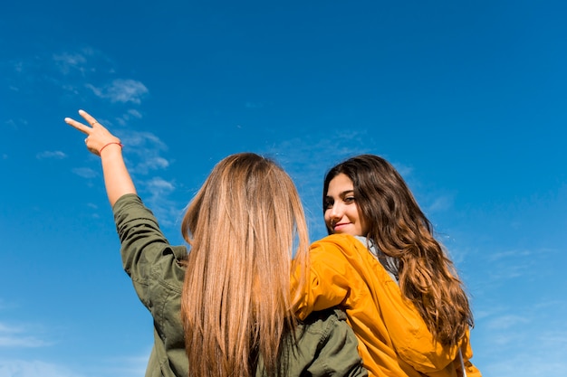 Vista posterior de la niña sonriente con su amiga gesticulando signo de victoria