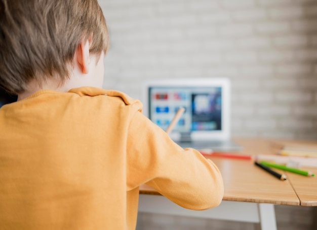 Foto gratuita vista posterior del niño aprendiendo de la computadora portátil en casa