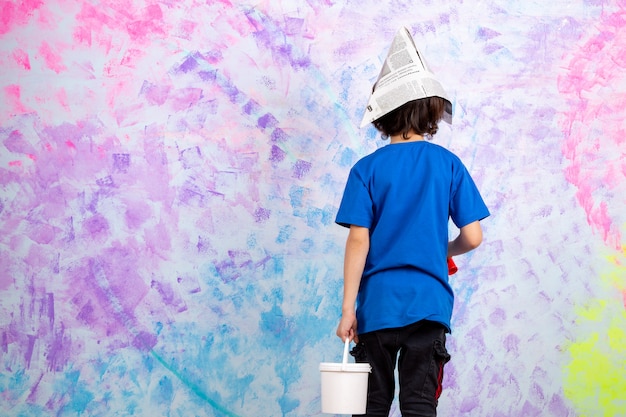 Foto gratuita vista posterior del niño pequeño en camiseta azul con pincel y pinturas multicolores