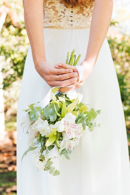 Vista posterior de una novia con la mano detrás de su espalda sosteniendo un ramo de flores