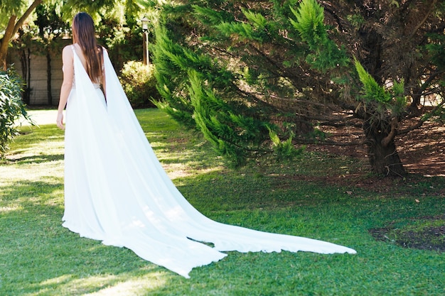 Vista posterior de una novia en vestido largo blanco caminando en el parque