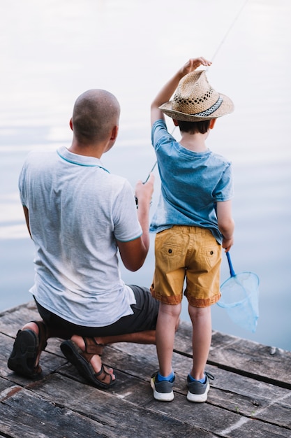 Foto gratuita vista posterior de padre y niño de pesca en el lago