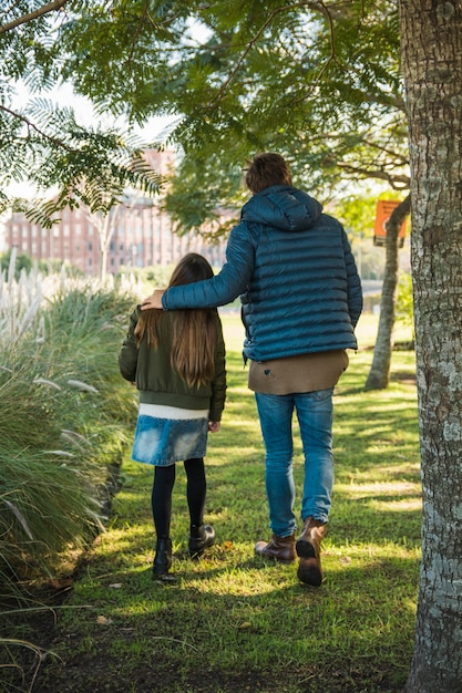 Vista posterior de un padre y su hija caminando sobre hierba