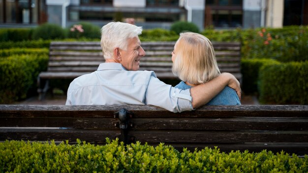 Vista posterior de la pareja de ancianos abrazados al aire libre en un banco