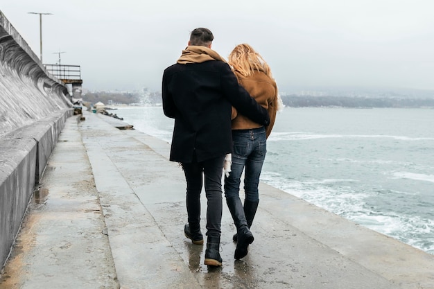 Foto gratuita vista posterior de la pareja caminando abrazados por la playa en invierno