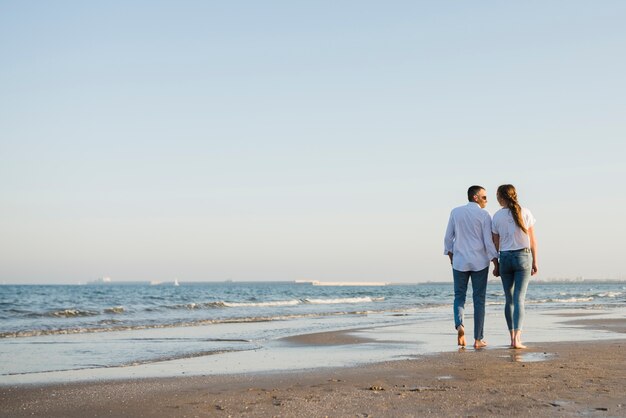 Vista posterior de la pareja caminando en la playa de arena