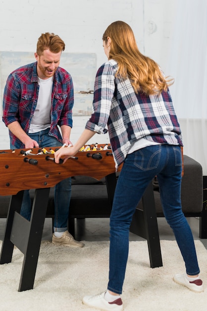 Vista posterior de la pareja disfrutando del juego de futbol de mesa en casa.