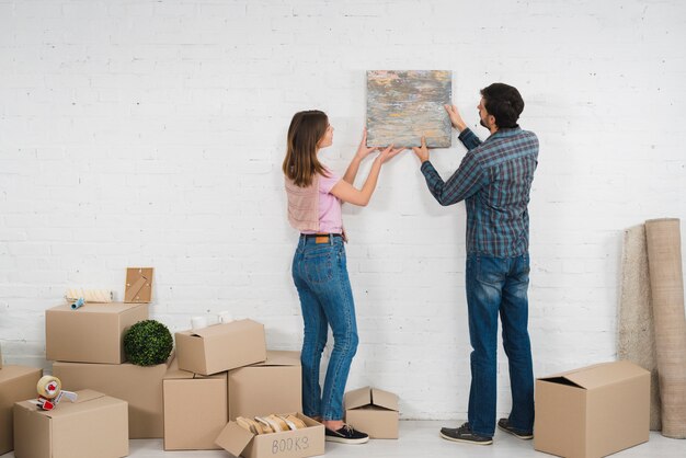 Vista posterior de una pareja joven colocando un marco de fotos en una pared blanca con cajas de cartón