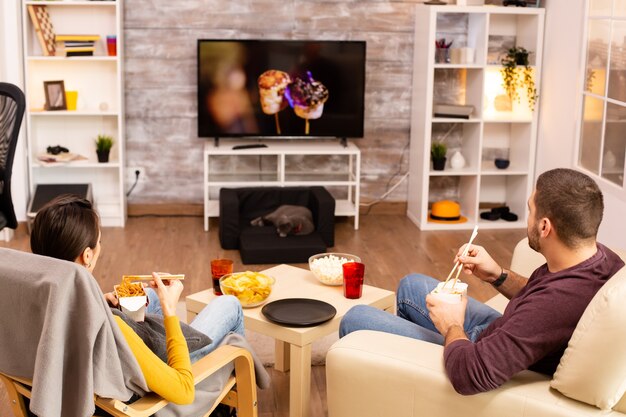 Vista posterior de la pareja en la sala de estar viendo una película en la televisión mientras come comida para llevar