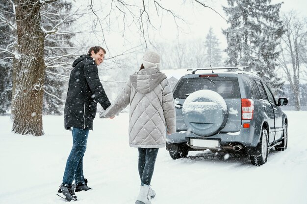 Vista posterior de la pareja sonriente disfrutando de la nieve durante un viaje por carretera