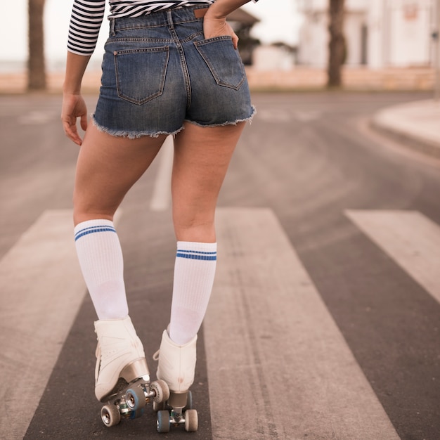 Vista posterior de una patinadora con la mano en el bolsillo de pie en la carretera