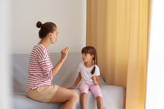 Vista posterior del patólogo del habla que enseña la pronunciación correcta de los sonidos de la hija de un niño pequeño, fisioterapeuta que trabaja en defectos del habla o dificultades con una niña pequeña en el interior.