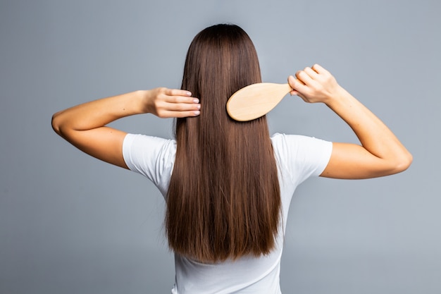 Vista posterior de peinar el cabello sano largo y liso femenino aislado en gris