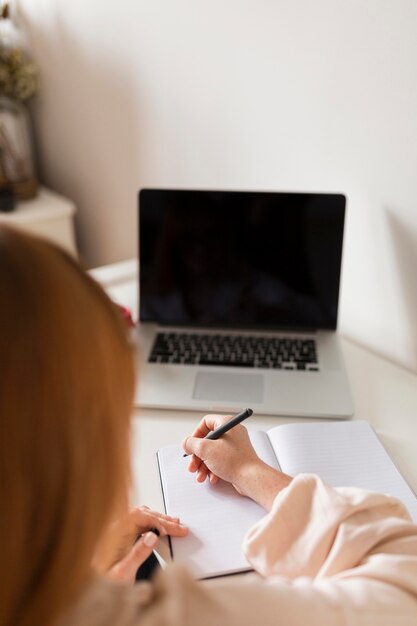 Vista posterior de la profesora sosteniendo una clase en línea con computadora portátil y agenda