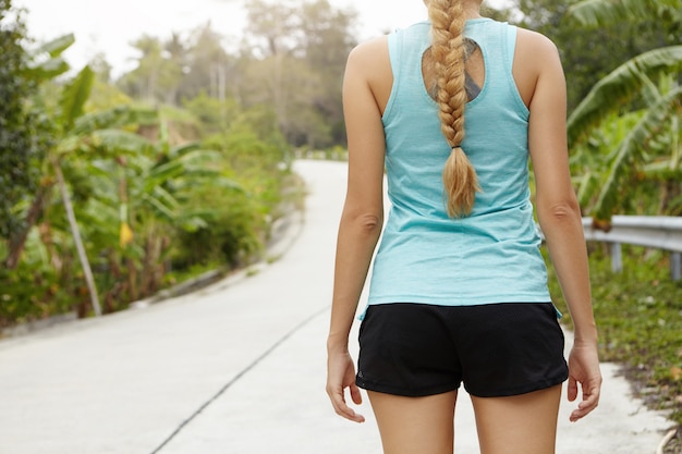 Foto gratuita vista posterior recortada del corredor femenino con trenza larga que descansan después de correr por la mañana al aire libre.
