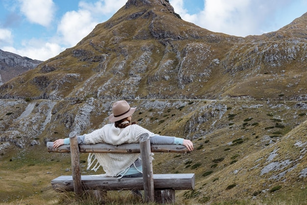 Vista posterior de la señorita con sombrero y cálido poncho en el paisaje montañoso Durmitor Montenegro