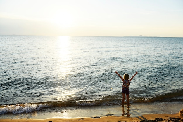 Foto gratuita la vista posterior de la silueta de la muchacha caucásica joven con los brazos levantó solamente en la playa