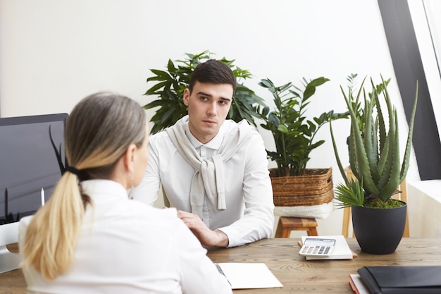 Vista posterior del solicitante de empleo de mujer de mediana edad irreconocible con cabello gris sentado frente a un empresario masculino joven y guapo durante la entrevista. Personas, negocios, ocupación y carrera.