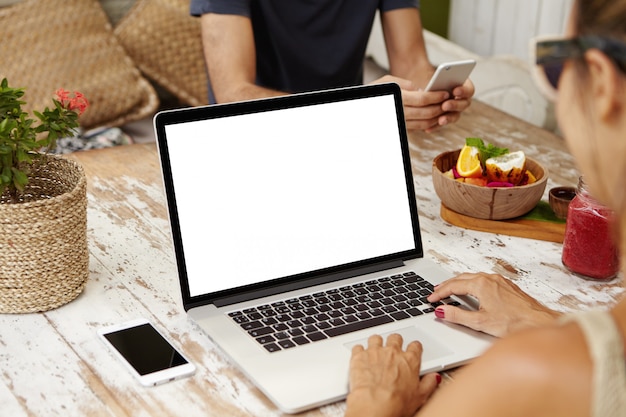 Vista posterior del teclado independiente femenino en la computadora portátil mientras se trabaja de forma remota. Mujer elegante en tonos usando la computadora portátil