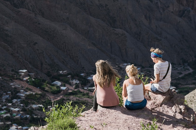 Vista posterior de tres mujeres sentadas en la cima de la montaña