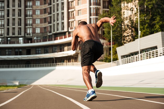 Vista posterior del velocista afroamericano que comienza en la pista de atletismo