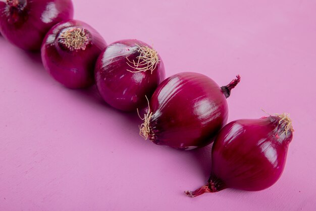 Vista de primer plano de cebollas rojas enteras sobre fondo morado con espacio de copia