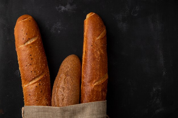 Vista de primer plano de diferentes tipos de baguette en el lado izquierdo y fondo negro con espacio de copia