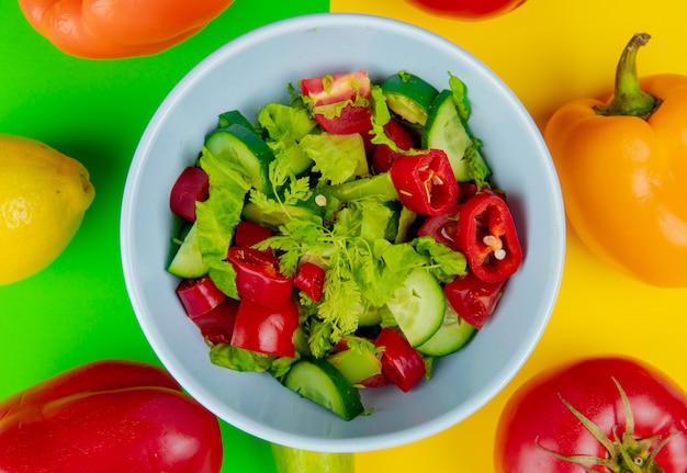 Vista de primer plano de ensalada de verduras en un tazón con pimiento tomate limón sobre fondo verde y amarillo