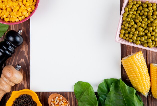 Vista de primer plano de maíz cortado con semillas de maíz semillas de pimienta negra guisantes verdes espinacas y bloc de notas sobre superficie de madera con espacio de copia