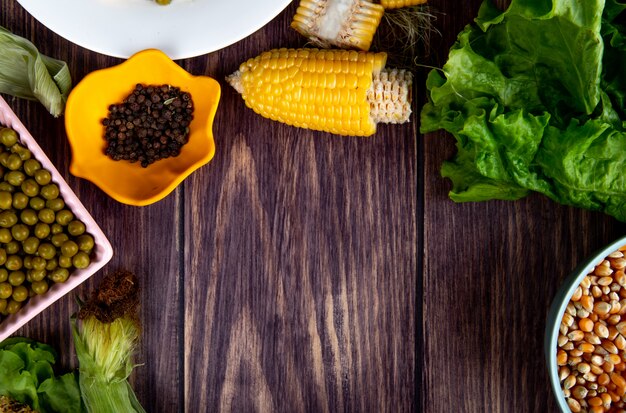 Vista de primer plano de maíz cortado y tazón de pimienta negra con lechuga semillas de maíz en superficie de madera con espacio de copia