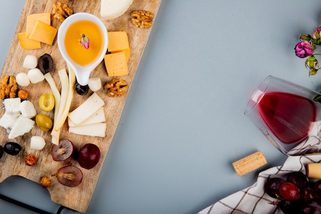 Vista de primer plano de mantequilla con queso uva nueces en tabla de cortar y vaso de corchos de vino flores en blanco con espacio de copia