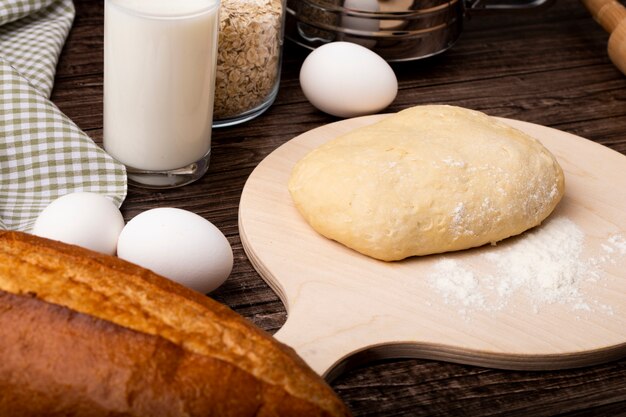 Vista de primer plano de masa con harina en tabla de cortar y leche de huevos sobre fondo de madera