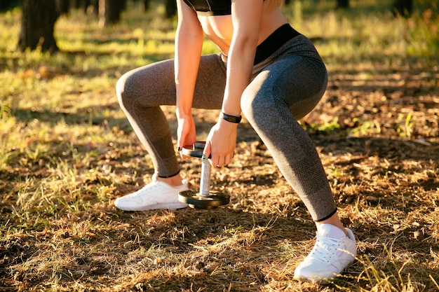 Vista de primer plano de mujer de deportes, levantando una pesa, mientras se ejercita en el parque.