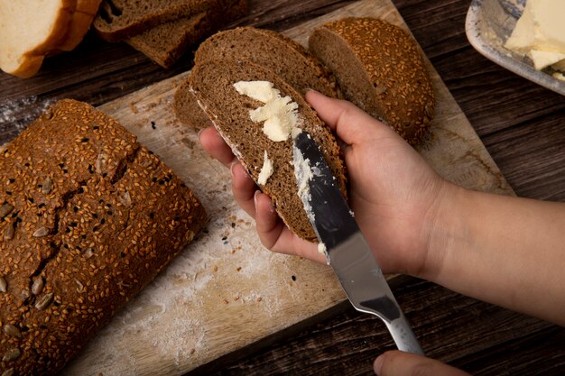 Vista de primer plano de mujer hans untando la mantequilla sobre el pan con un cuchillo y cortar el pan en la superficie de madera y fondo