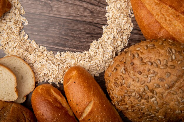 Vista de primer plano de panes como baguette blanco con copos de avena sobre fondo de madera