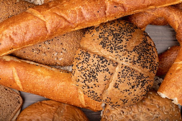 Vista de primer plano de panes como semillas de amapola baguette mazorca bagel y otros sobre fondo de madera