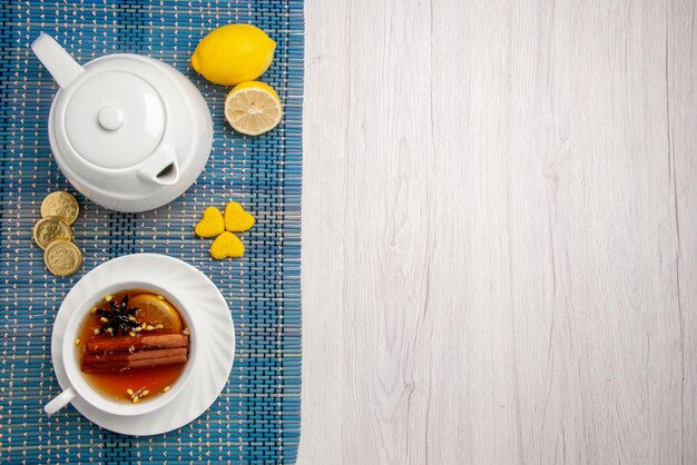 Vista de primer plano superior dulces y una taza de té una taza de té de hierbas con limón y canela tetera de limón diferentes dulces en el mantel a cuadros en el lado izquierdo de la mesa