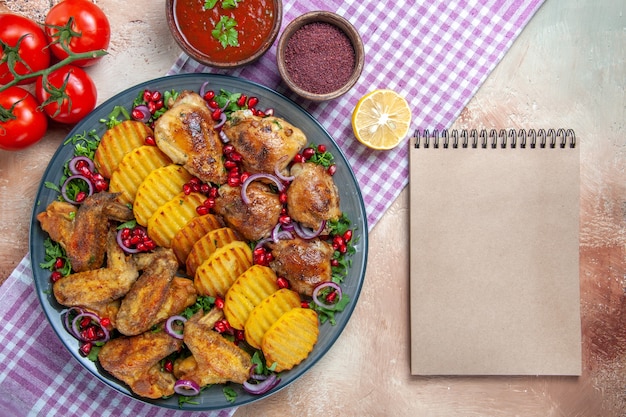 Vista de primer plano superior plato alitas de pollo patatas tomates salsa especias en el cuaderno de mantel