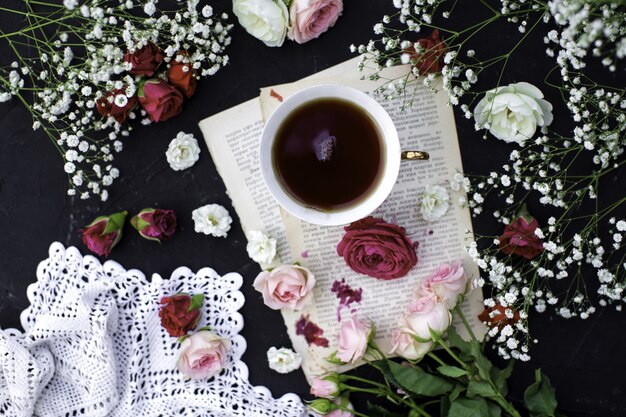 Una vista de primer plano superior taza de té caliente junto con coloridas rosas en la superficie oscura