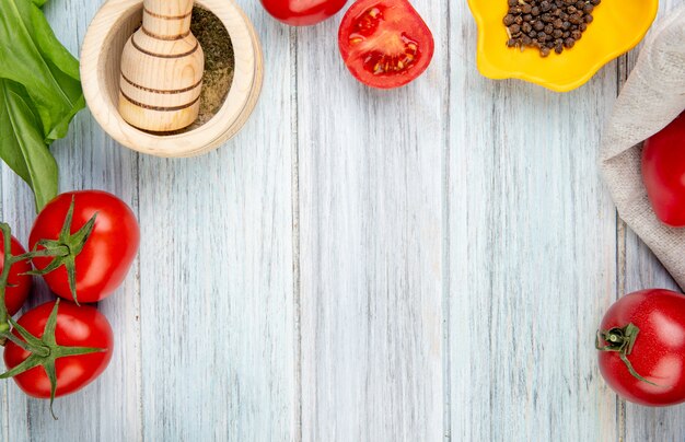 Vista de primer plano de verduras como espinacas de tomate con pimienta negra trituradora de ajo en la mesa de madera con espacio de copia