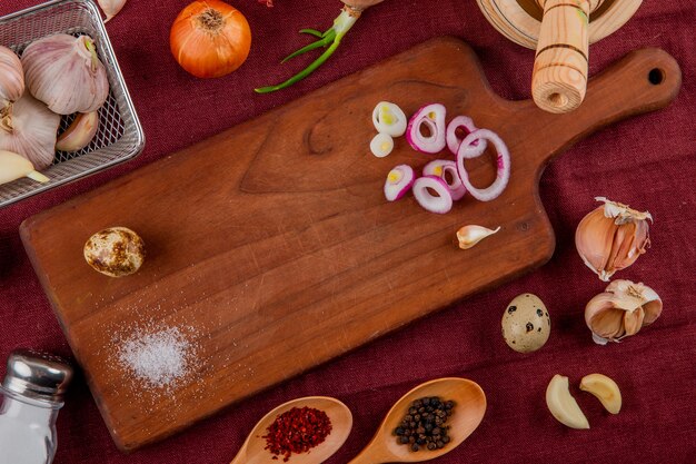 Vista de primer plano de verduras como huevo de cebolla en tabla de cortar ajo con sal y especias sobre fondo de Borgoña