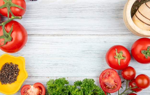 Vista de primer plano de verduras como tomate cilantro con pimienta negra trituradora de ajo en mesa de madera con espacio de copia