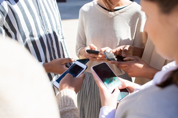 Vista recortada de jóvenes que usan teléfonos inteligentes