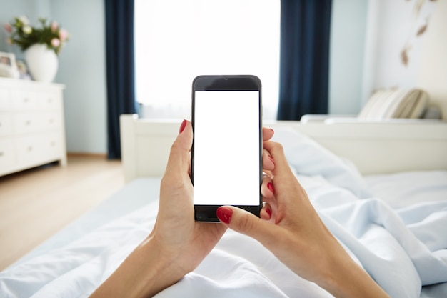Vista recortada de manos femeninas sosteniendo un teléfono inteligente con pantalla en blanco