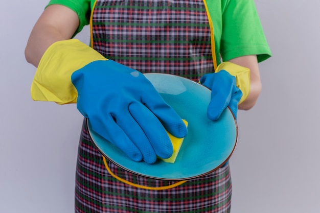 Vista recortada de la mujer vestida con delantal y guantes de goma con vajilla en la placa de lavado de manos