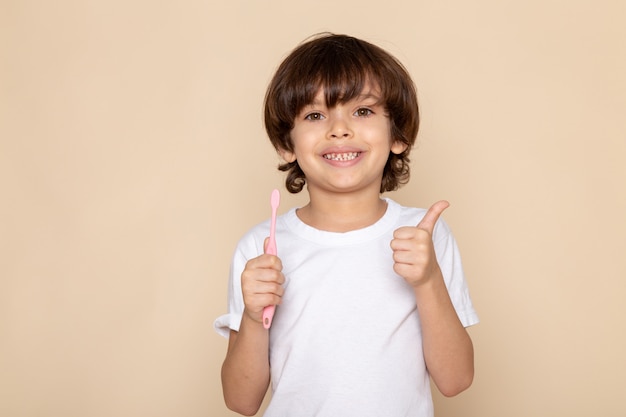 Vista de retrato frontal, niño sonriente lindo adorable dulce en camiseta blanca en pared rosa