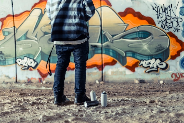 Vista de sección baja de artista parado cerca de la lata de aerosol frente a graffiti en la pared